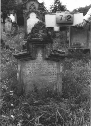 Grabstein 72 (Index: 99799551) Material: Sandstein Zustand: stark verwittert, abgerieben, weitgehender Textverlust Maße HxBxT: 89x50x19 cm Beschreibung: Stele, flache Schultern, Mittelerhöhung, Verdachung mit Palmettenaufsatz, Schriftfeld eingetieft Symbolik: floral: Grabstein 72