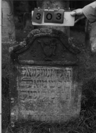 Grabstein 303 (Index: 100107712) Material: heller Sandstein Zustand: stark verwittert und versalzen, weitgehender Textverlust Maße HxBxT: 95x65x14 cm Beschreibung: Stele mit geschwungenem Korbbogenabschluß, Schriftfeld rechteckig eingetieft Symbolik: Levitenkanne Besonderheit: Kindergrab: Grabstein 303