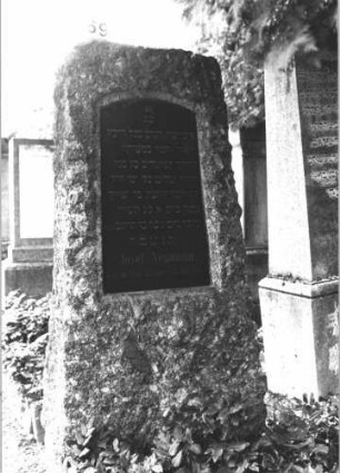 Grabstein 69 (Index: 100114386) Material: Granit mit schwarzer Marmorplatte Zustand: gut Maße HxBxT: 185x83x45 cm Beschreibung: grob stelenhaft behauener Stein, Schrifttafel mit Segmentbogen: Grabstein 69