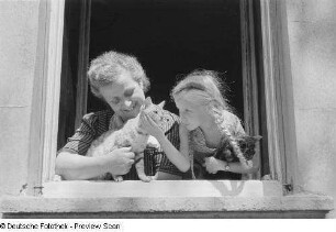 Frau und Mädchen mit Katzen an einem Fenster