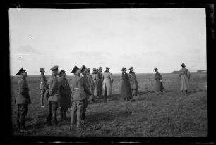 Nicht identifizierbare Ortschaft in Nordfrankreich oder Belgien: Offiziere mit Schirmmütze auf einem Feld mit Blick in den Himmel (Distanzaufnahme)