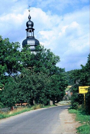 Straße mit Ortsschild, Bäume, Kirchturmspitze