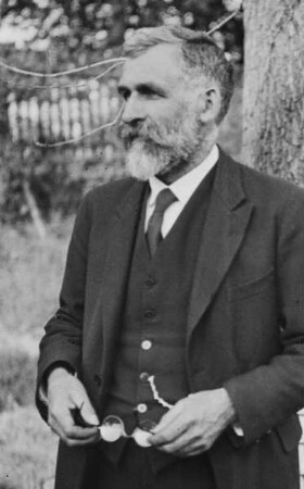 Porträt des Richard Hamann mit abgenommener Brille in einem Garten