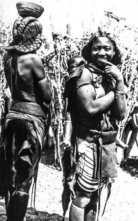 Zwei Indigene mit Kind : Zwei Indigene aus Ostafrika in traditioneller Kleidung. Einer von ihnen trägt ein Kind auf dem Rücken.