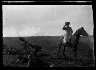 Nicht identifizierbare Gegend in Nordfrankreich oder Belgien: Husar zu Pferd neben in Schlachtreihe liegenden Soldaten mit Pickelhaube