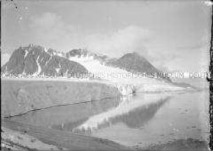 Dunkle Bergreihe mit Schneefurchen, Gletscher, Steilküste und spiegelglattem Fjord, Nordlandreise, Norwegen