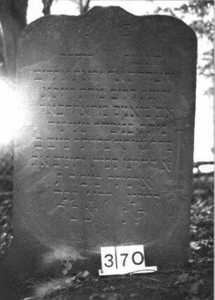 Grabstein 370 (Index: 99898369) Material: Sandstein Zustand: gut erhalten, stellenweise leicht angewittert Maße HxBxT: 112x71x8 cm Beschreibung: Stele mit Kielbogenabschluss, von der abgebrochenen (oder abgeflachten) Spitze herabhängende, eingeritzte Blüte, Rahmen durch eingeritzte Rankenornamente Symbolik: Blüte, Ranken: Grabstein 370