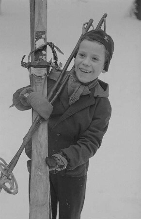 Kinder beim Ski- und Schlittenfahren, Junge mit Ski nach der Abfahrt
