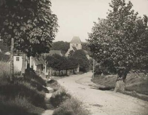 Dorf Garzin im Westen der Märkischen Schweiz (Brandenburg). Ansicht der Dorfstraße. Im Bildhintergrund die aus dem 13. Jh. stammende Feldsteinkirche; eine einschiffige Saalkirche mit vorgelagerten Turm