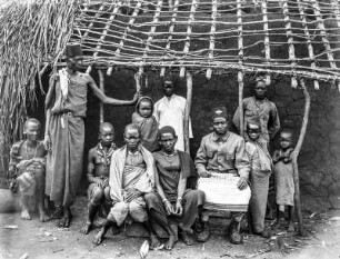 Gruppe von Dorfbewohnern : Ein Gruppenportrait indigener Dorfbewohner aus der Steppe am Pare-Gebirge, unter ihnen vermutlich Jumben (Dorfvorsteher), vor einer Hütte. Zwei der Portraitierten tragen einen Tarbusch.