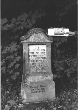Grabstein 57 (Index: 100106543) Material: Sandstein, Schriftplatte Marmor Zustand: bewachsen Maße HxBxT: 147x54x19 cm Beschreibung: Stele mit Konvexbogenabschluß mit Verdachung, Schriftplatte eingelassen, getreppter Sockel: Grabstein 57