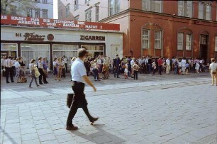 DDR. Straßenbild mit Wartenden an einer Straßenbahnhaltestelle und Spruchband "Alle Kraft für die Festigung der Arbeiter- und Bauern-Macht" an einem Flachbau