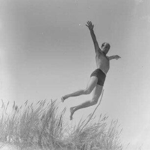 Mann in Badehose springt am Strand
