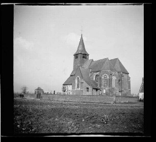 Tourmignies (Dep. Nord, Frankreich): "Kirche [Saint-Pierre-d'Antioche] von Tourmignies" mit Friedhof, im Vordergrund ein Feld (Rückansicht, Distanzaufnahme)