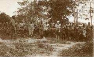 Angekettete Gefangene, darunter ein "Albino-Zauberer", bewacht von afrikanischen Soldaten der Schutztruppe