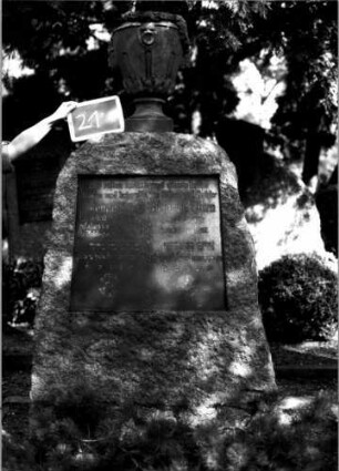 Grabstein 21 (Index: 100110062) Material: Granit Zustand: gut Maße HxBxT: 190x83x45 cm Beschreibung: konische Stele, Korbbogenabschluß, Schriftplatte rechteckig Symbolik: Eisernes Kreuz mit Davidstern und Lorbeerkranz, stilisierte Blüte, Urne mit Kranz als Aufsatz Besonderheit: Doppelgrab: Grabstein 21