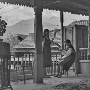 Veranda eines Wohnhauses in Bansko. Zwei junge Frauen in bulgarischer Tracht üben das Handwerk des Spinnens aus