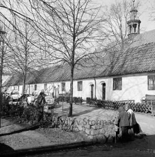 Gottesbuden: südliche Reihe: Jägerzaun, Ruhebank: davor Weg, alte Frau, Autos, Wäscheleine: rechts dahinter Dachreiter von Schlosskirche: im Vordergrund zwei Kinder