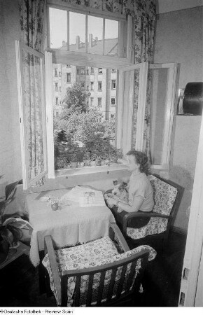Frau, an einem offenen Fenster sitzend