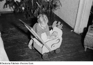 Porträt eines kleinen Mädchens mit Puppenwagen vor einem Weihnachtsbaum