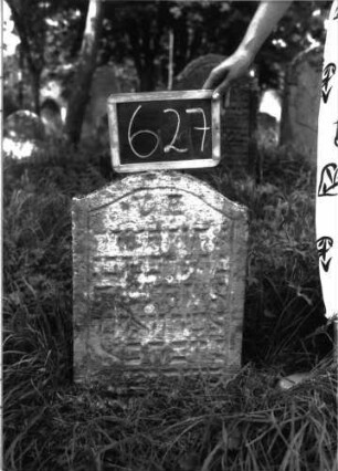 Grabstein 627 (Index: 100104994) Material: Sandstein Zustand: stark verwittert, eingesunken, teilweiser Textverlust Maße HxBxT: 63x42x8 cm Beschreibung: Stele, Konvexbogenabschluss, Schriftfeld eingetieft: Grabstein 627
