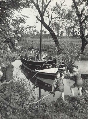 Zwei Jungen betrachten ein Segelboot, das auf einem Priel liegt