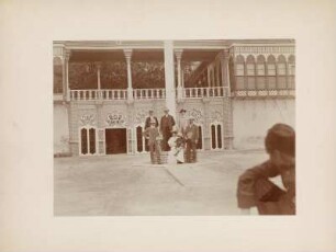 Gruppenportrait : Portraitaufnahme von einer Frau mit Kind und fünf Männern in einem Innenhof in Bagdad. Rechts vorne der Geograph Hugo Grothe (1869-1954).
