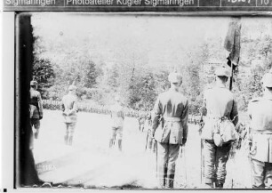 Kronprinz Wilhelm (Rückenansicht mit Mütze und Säbel) bei einem Dankgottesdienst an der Haquette-Ferme bei Lançon am 9. Juli 1915, auf einer Wiese angetretene Soldaten, im Hintergrund das Hüttenlager des 124.Infanterieregiments
