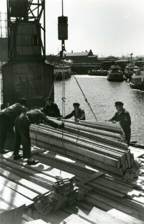 Hamburg. Hafen, Dalmannkai. Schauerleute entladen ein Frachtschiff. Das Holz wird mittels eines Hafenkranes von Bord gehievt