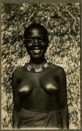 Frontale Porträtaufnahme einer jungen afrikanischen Frau vor einer Hütte