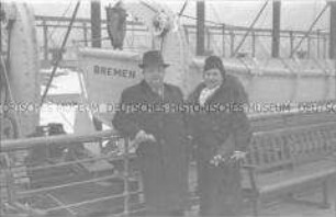 Passagiere (Ehepaar) an Deck des Hochseepassagierdampfers "Bremen", vor einem Rettungsboot an der Reling lehnend