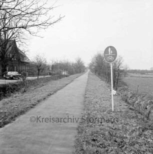 Radwanderweg auf der Trasse der Südstormarnschen Kreisbahn: vorn rechts Straßenschild: links Pkw vor Bauernhaus