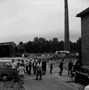 Stadtwerke Bad Oldesloe: Gaswerk: Lübecker Straße: Sprengung des Schornsteins des abgerissenen Kraftwerks: rechts Gebäudeecke und Pkw: dahinter Schornstein mit Gastank: im Vordergrund Polizist, Arbeiter und weitere Personen: links VW-Bus: hinten Bauschutt: links teilweise abgerissenes Gebäude: hinten Bäume: 10. Juni 1971