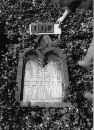 Grabstein 112 (Index: 99792204) Material: Sandstein Zustand: verwittert mit Textverlust Maße HxBxT: 86x48x11 cm Beschreibung: Stele, eingezogener Spitzbogenabschluß, Schriftfeld eingetieft Symbolik: Maßwerk: Grabstein 112