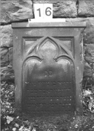Grabstein 16 (Index: 100105954) Material: Sandstein Zustand: unten abgebrochen und am rechten Rand beschädigt, verwittert Maße HxBxT: 58x44x18 cm Beschreibung: Stele, mit Abdeckplatte, Schriftfeld eingetieft mit Spitzbogenabschluß Symbolik: Maßwerk: Grabstein 16