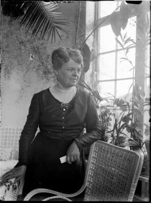 Wohnung der Familie Knochenhauer, Wintergarten? Fanny Knochenhauer, an einem Korbstuhl aufgestützt stehend : Kattowitz, Friedensstraße 2. Wohnung der Familie Knochenhauer, Wintergarten? Fanny Knochenhauer, an einem Korbstuhl aufgestützt stehend