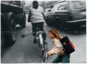 Kleines Mädchen auf dem Fahrrad, im Hintergrund Plakat (Altersgruppe bis 14)