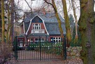 Tremsbütteler Weg (57): traufständige Villa aus Backstein mit Mansarddach: Straßenfront, links geschweifter Zwerchgiebel, Auslucht, Altan: Giebelseite, unten Eingangsvorbau, oben an Giebel Fuß: davor Vorgarten, Auffahrt, vorne Gartentor aus Schmiedeeisen, Feldsteinmauer, Bäume