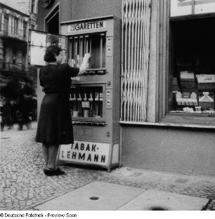Berlin. Tabakwarengeschäft Lehmann. Besitzerin bestückt einen Zigarettenautomaten vor dem Geschäft