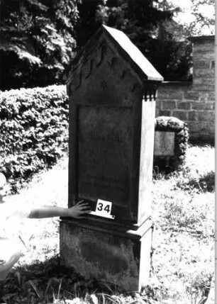 Grabstein 34 (Index: 100081733) Material: Sandstein Zustand: leicht verwittert Maße HxBxT: 173x63x30 cm Beschreibung: giebelart. Abschluß m. Verdach. , rechteck. Schriftfeld eingetieft, profiliert. Sockel Symbolik: Sternchen, gestelztes Rundbogenfries unter Abschluß: Grabstein 34