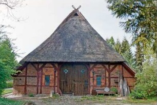 Hauptstraße 103: Fachhallenhaus mit Reetdach: Giebelseite Wirtschaftstrakt mit Scheunentor, Giebelzier Pferdeköpfe: vor Hauswand Bank, Vorplatz mit Pflasterung: 9. Mai 2003