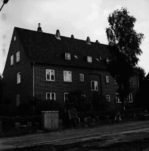 Hebbelstraße: Ausbau: vorn unbefestigte Straße, Stapel mit Gehwegplatten und Stromverteilerkasten: dahinter Wohnhäuser der Gemeinnützigen Baugenossenschaft Bad Oldesloe mit Vorgärten