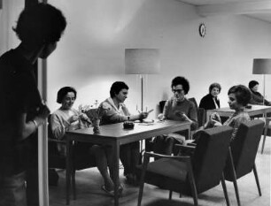 Müttergenesungsheim. Frauen sitzen im Aufenthaltsraum und verbringen ihre Freizeit mit Karten spielen und stricken.