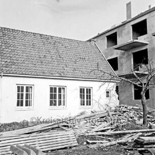 Polizeiwache: Mühlenstraße: links halb abgebrochener Anbau: rechts hinten mehrgeschossiges Wohn- und Geschäftshaus im Rohbau: vorn rechts Baum: daneben Bretterhaufen