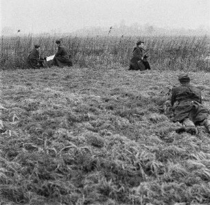 Deutsche Demokratische Republik. Grenze zwischen BRD und DDR. Offizier und Grenzpolizist bei einer Lagebesprechung mit Karte im Gelände, abseits zwei Grenzposten zur Sicherung des Abschnittes