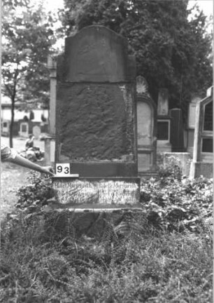 Grabstein 93 (Index: 100114231) Material: Sandstein Zustand: verwittert, Schriftplatte fehlt Maße HxBxT: 190x81x36 cm Beschreibung: konische Stele, getreppter Sockel, unterer Sockel runsticaartig, eingezogener Konvexbogenabschluß Besonderheit: Doppelgrab: Grabstein 93