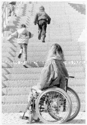 Zwei Kinder laufen eine Treppe hoch, unten sitzt eine junge Frau im Rollstuhl und schaut ihnen nach (Sonderthema: Traum-Bilder)