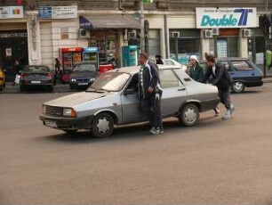 Drei Männer schieben ein defektes "Dacia" Auto über eine Kreuzung in Bukarest