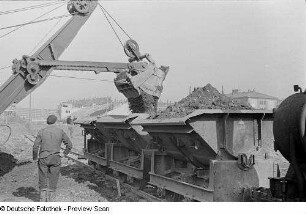 Verladen von Steinen und Erde mit Hilfe eines Baggers auf eine Trümmerbahn