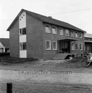 Amtsverwaltung: Hauptstraße: Amtshaus vor Fertigstellung: im Vordergrund Zaun: vorn unbefestigte Außenanlagen: rechts Außentreppe: darauf und daneben Baumaterial: dahinter Leiter an Wand: hinten rechts ehemalige Volksschule
